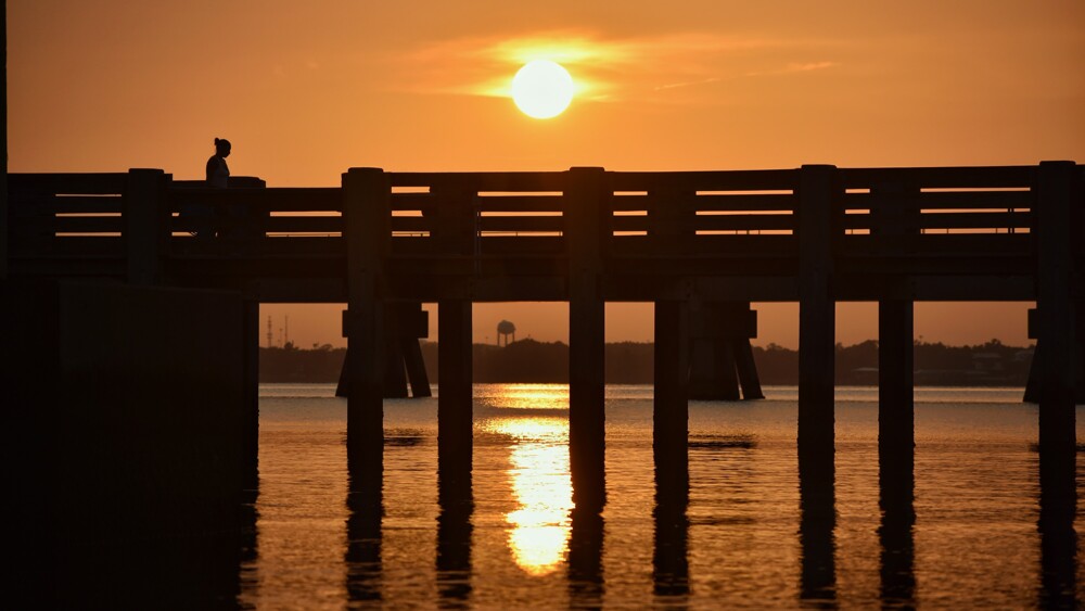 Angler in silhouette on a pier at sunset